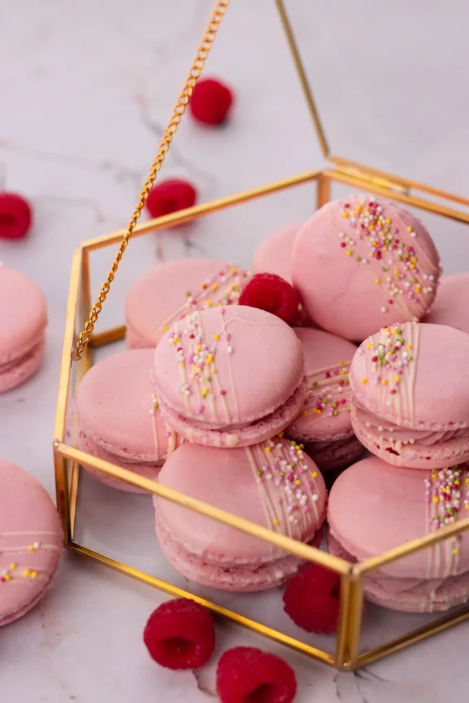 Różowe makaroniki z posypką w złotej szkatułce na marmurowym tle